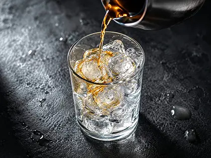 Gourmet ice kocke u čaši dok se piće sipa preko kristalno čistog leda iz gornjeg ugla